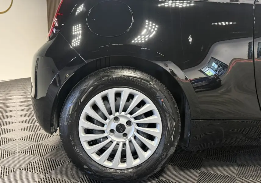 Gros plan sur la roue arrière gauche de la Fiat 500 électrique noire 2024 avec jante acier 15 pouces et logo central.
