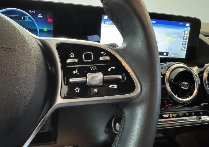 Gros plan sur la partie gauche du volant cuir du Mercedes GLA 250 e gris foncé, avec commandes tactiles et écran tactile en arrière-plan.