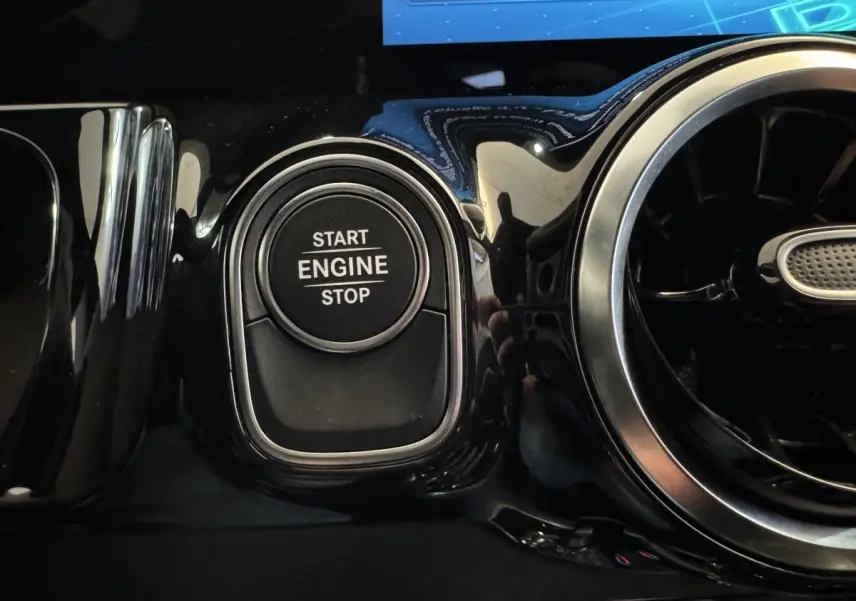 Gros plan sur le bouton Start Engine Stop noir entouré de chrome dans l’habitacle brillant gris foncé d’une Mercedes GLA 250 e Business Line 2023.