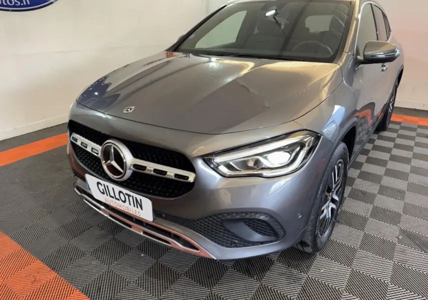 Mercedes GLA 250 e Business Line gris foncé vue 3/4 avant avec phares LED allumés et calandre chromée.