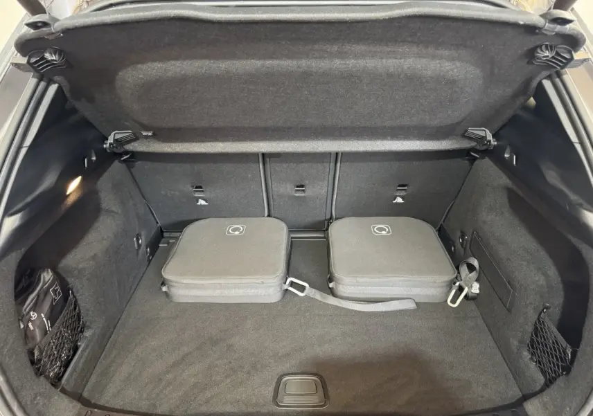 Vue plongeante sur le coffre ouvert gris foncé du Mercedes GLA 250 e Business Line avec deux sacs de rangement noirs.