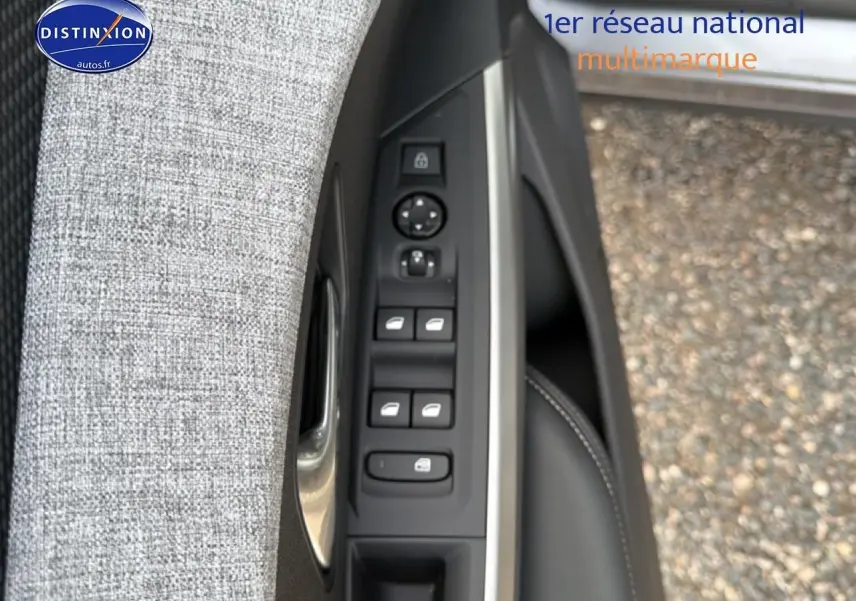 Gros plan sur la commande des vitres électriques et rétroviseurs côté conducteur avec tissu gris et garniture noire.