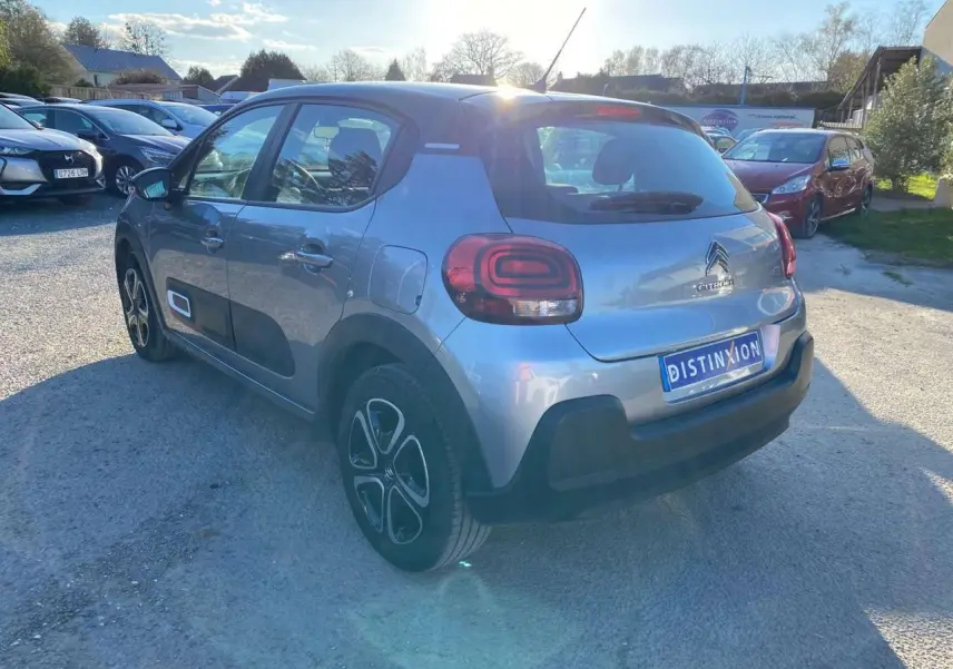 Vue 3/4 arrière droite d'une Citroën C3 gris Artense avec toit noir et protections latérales noires sur un parking.