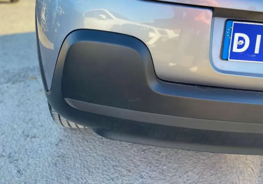 Gros plan sur le pare-chocs arrière gris Artense d'une Citroën C3 2022, avec partie inférieure noire et plaque d'immatriculation partielle.