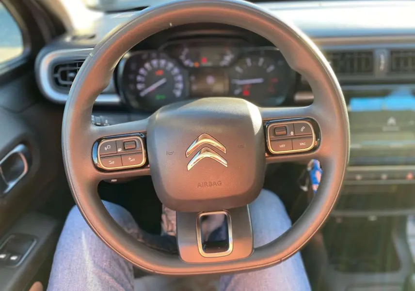 Vue rapprochée du volant noir de la Citroën C3 2022 avec commandes intégrées et tableau de bord flou en arrière-plan.