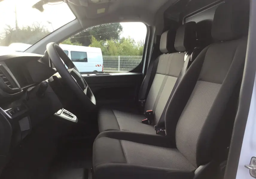 Vue intérieure côté conducteur du Fiat Scudo Fourgon blanc 2024, montrant les sièges avant en tissu gris et noir.