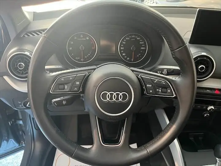 Vue rapprochée du volant noir Audi Q2 2020 avec commandes intégrées et tableau de bord visible en arrière-plan.