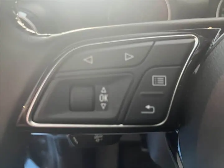 Boutons de commande multifonction sur le volant d'un Audi Q2 gris Daytona, vue rapprochée côté gauche.
