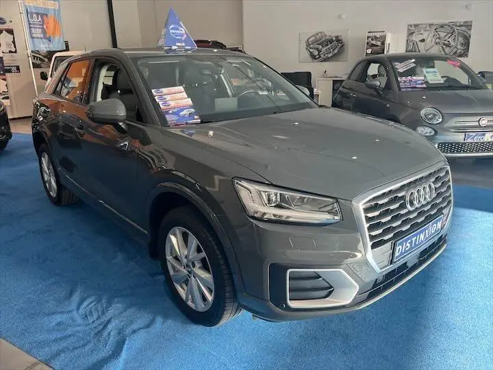 Audi Q2 gris Daytona métal vue 3/4 avant droit en showroom avec affichage commercial sur le pare-brise