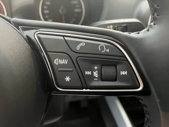 Gros plan sur les commandes multifonctions au volant d’un Audi Q2 35 TFSI gris Daytona, boutons pour navigation et audio.