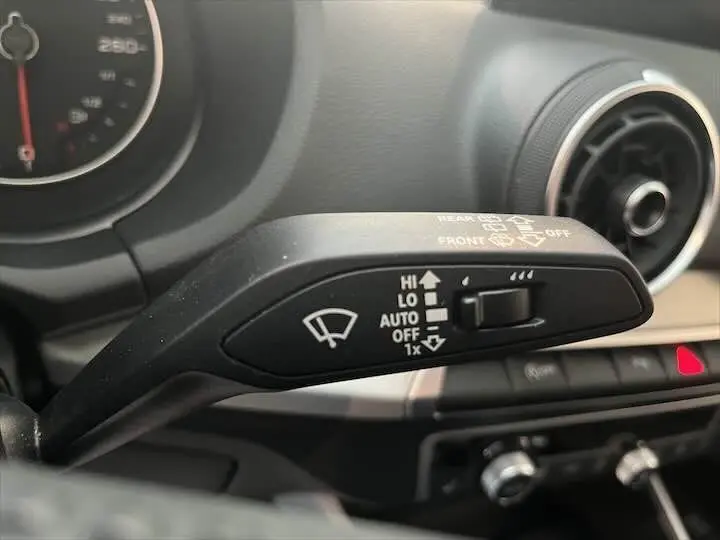 Gros plan sur la commande d'essuie-glace à gauche du volant dans l'Audi Q2 gris Daytona, tableau de bord en arrière-plan.