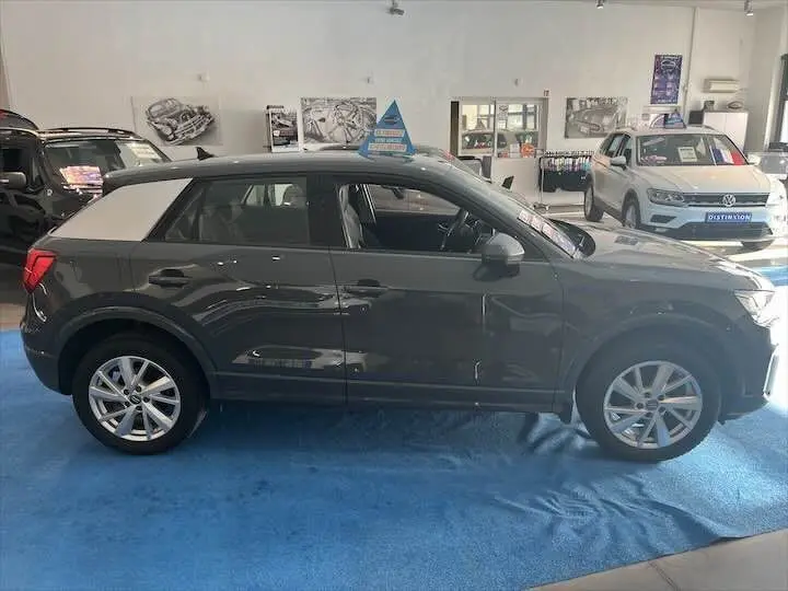 Audi Q2 35 TFSI gris Daytona métal vue de profil côté gauche avec toit contrasté blanc en showroom.