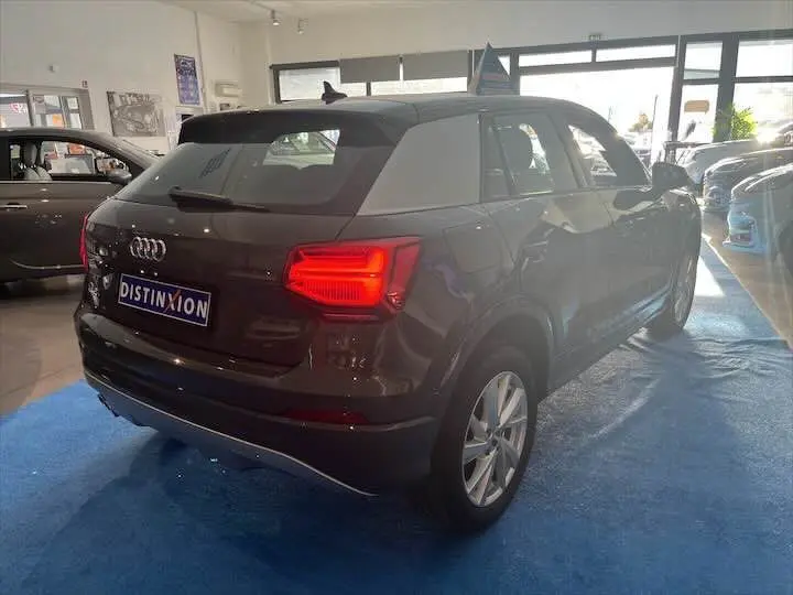 Audi Q2 gris Daytona metal vue 3/4 arrière droit en intérieur avec feux arrière allumés et plaque Distinxion.