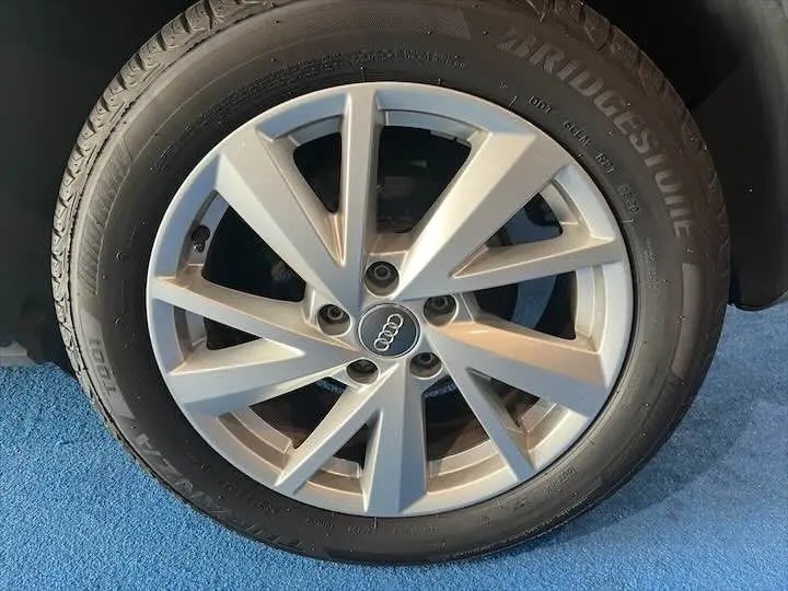 Gros plan sur la jante alliage argentée avec logo Audi du pneu Bridgestone d'un Q2 gris Daytona.