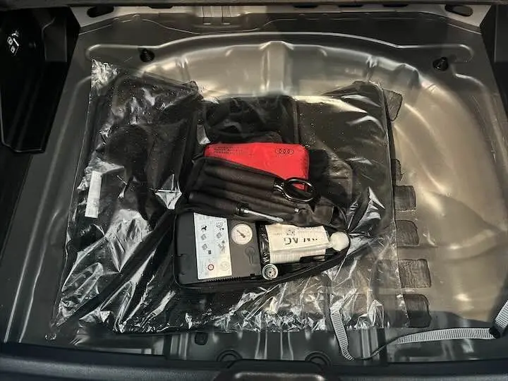 Vue plongeante sur le coffre d'un Audi Q2 gris Daytona Metal, montrant le kit de réparation pneus et accessoires rangés.