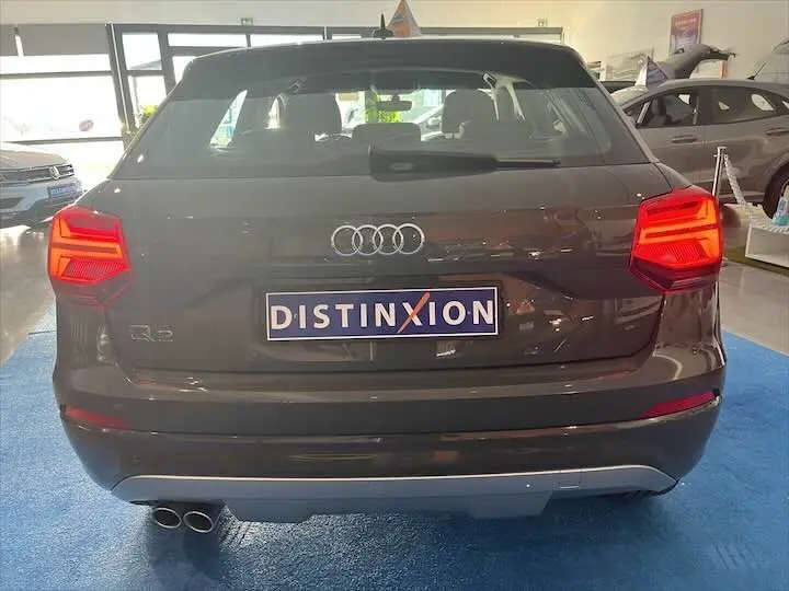 Vue arrière d'un Audi Q2 gris Daytona avec feux allumés et plaque Distinxion en concession.