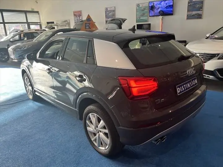 Audi Q2 gris Daytona métal vue 3/4 arrière droit en intérieur avec feux arrière allumés et toit noir contrasté