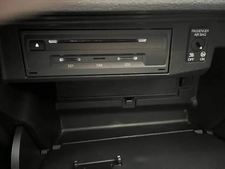 Gros plan sur le lecteur SD et SIM dans la boîte à gants d'un Audi Q2 gris Daytona 2020, avec indication airbag passager.