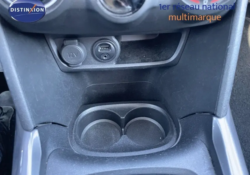 Gros plan sur la console centrale de la Peugeot 2008 blanche, montrant prise 12V, port USB et porte-gobelets noirs.