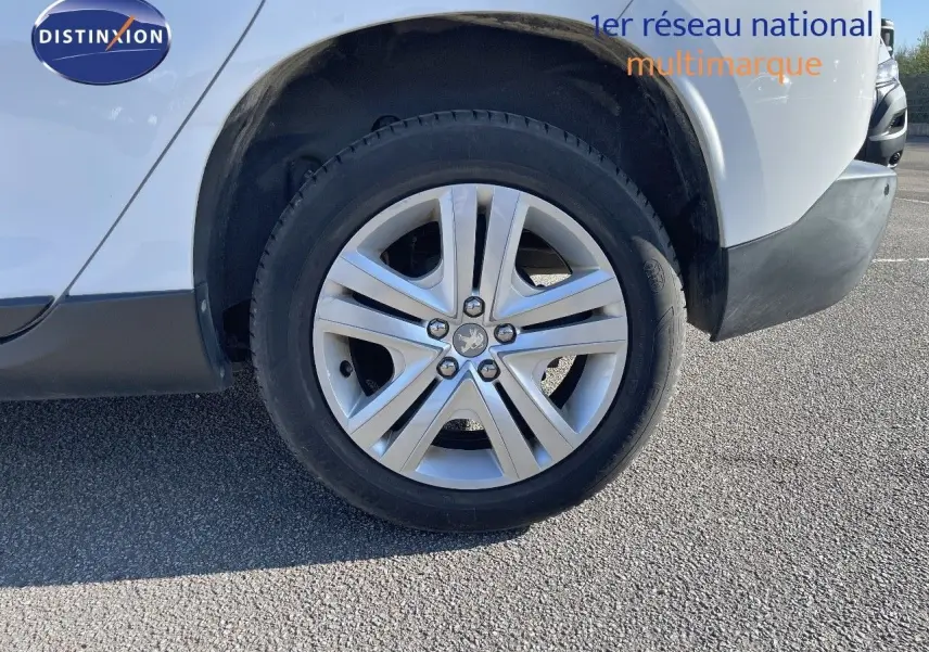 Gros plan sur la roue avant gauche d'un Peugeot 2008 blanc avec jante alliage et logo lion central.