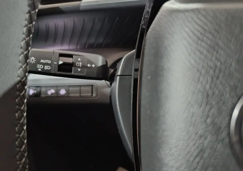 Gros plan sur la manette de commande d'éclairage à gauche du volant cuir noir du Citroën C3 hybride 2025.