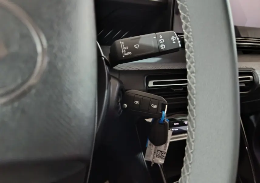 Vue rapprochée du volant cuir et de la clé insérée sur une Citroën C3 hybride noire, avec commandes au volant visibles.