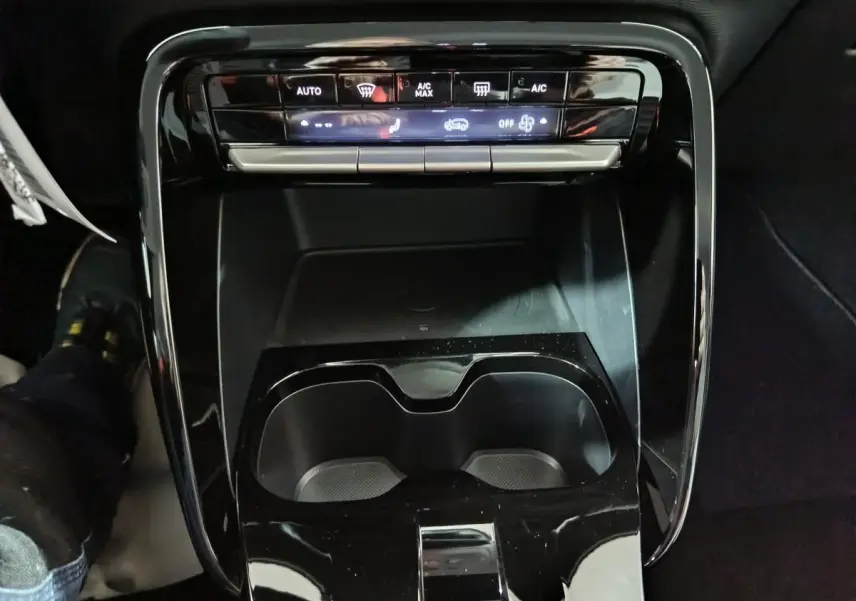 Vue rapprochée de la console centrale noire de la Citroën C3 hybride 2025, avec commandes climatisation et porte-gobelets.