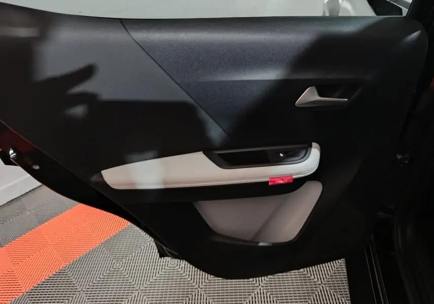 Vue intérieure côté gauche de la porte arrière noire de la Citroën C3 hybride avec accoudoir clair et poignée argentée.