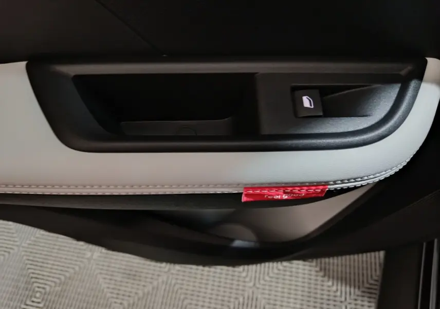 Gros plan sur la poignée intérieure côté droit de la porte noire et grise avec étiquette rouge "Feel Good" visible.