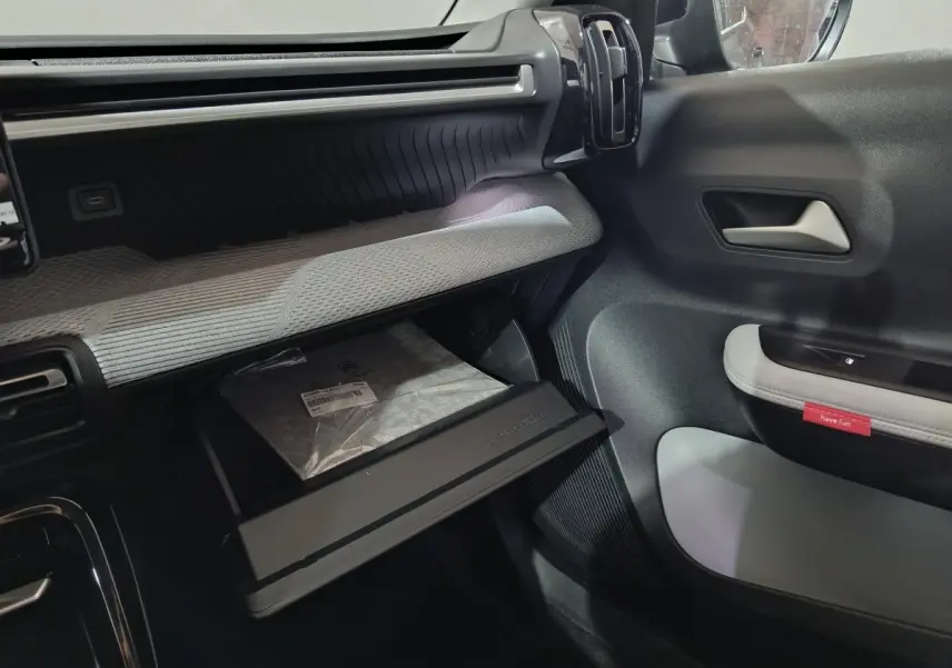 Intérieur de la Citroën C3 Hybride 2025, vue côté passager avec boîte à gants ouverte et garnitures grises et noires.