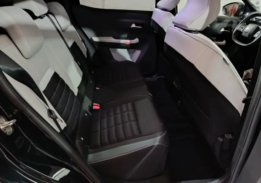 Vue intérieure arrière côté gauche de la Citroën C3 hybride 2025, sièges bicolores noir et gris clair avec détails matelassés.
