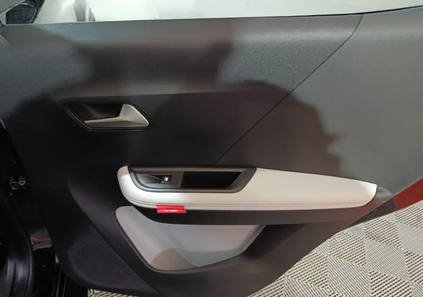 Vue intérieure du panneau de porte côté gauche de la Citroën C3 hybride 2025, avec accoudoir clair et bouton de fenêtre.
