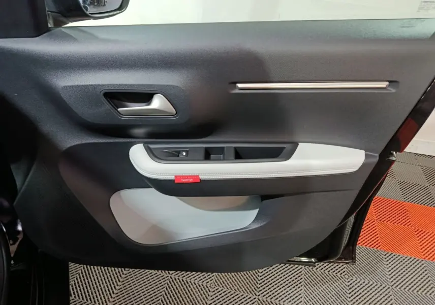 Vue intérieure du panneau de porte côté gauche de la Citroën C3 hybride noire, avec insert blanc et poignée argentée.