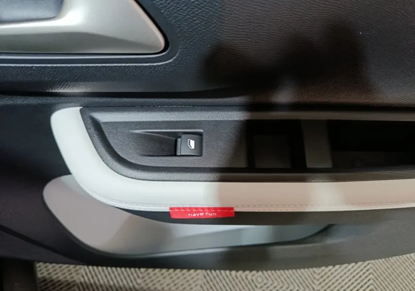 Détail de la poignée de porte intérieure côté gauche de la Citroën C3 hybride noire avec bouton de commande de vitre et étiquette rouge "have fun".