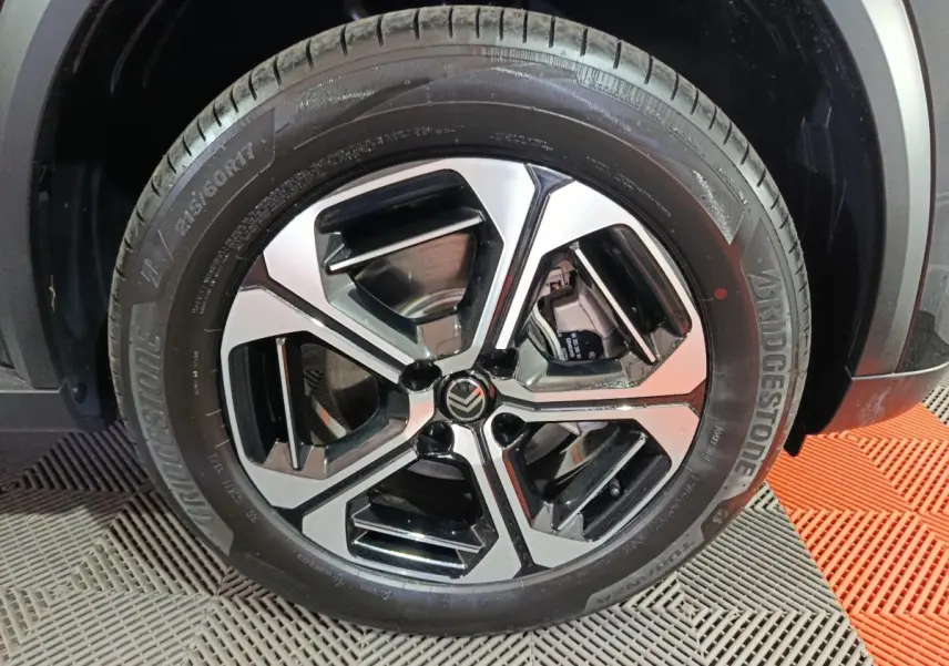 Gros plan sur la roue avant droite de la Citroën C3 hybride noire, mettant en valeur la jante alliage bicolore et le pneu Bridgestone.