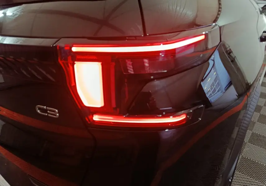Feu arrière droit allumé d'une Citroën C3 noire, vue rapprochée sur le logo et les lignes lumineuses distinctives.