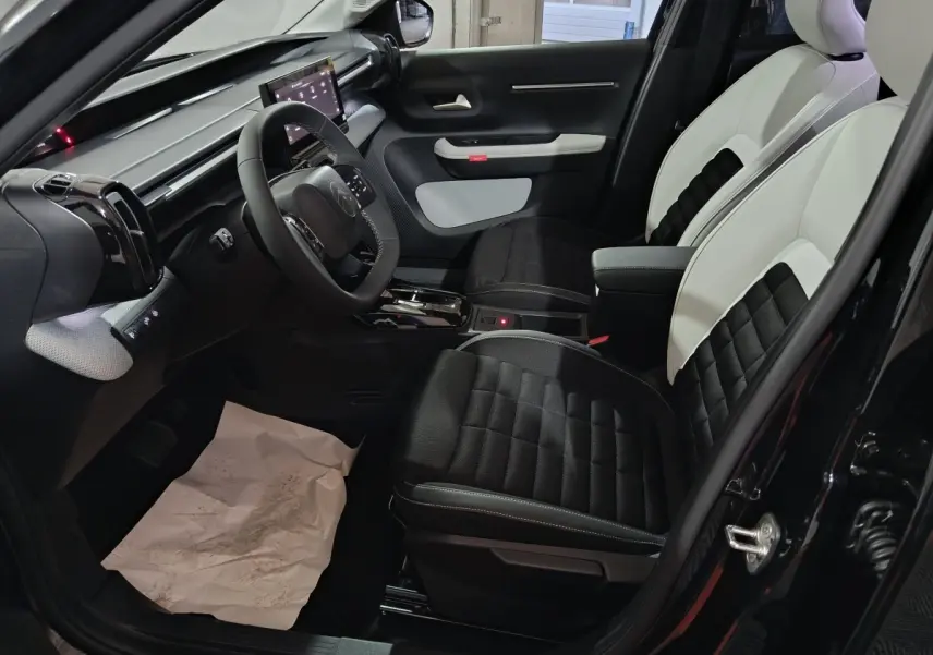 Vue intérieure côté conducteur de la Citroën C3 hybride 2025, sièges bicolores noir et blanc avec tableau de bord moderne.