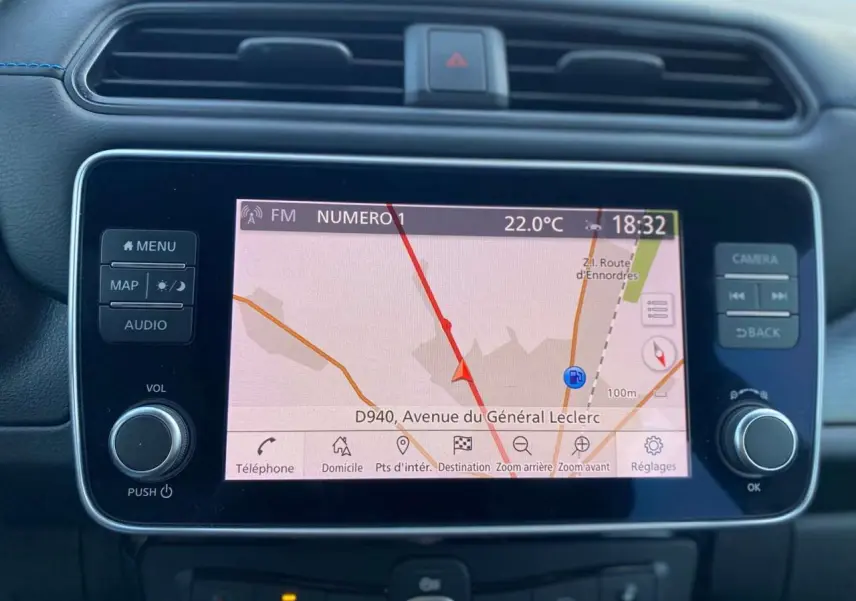 Gros plan sur l’écran tactile central du Nissan Leaf blanc 2020, affichant la navigation avec carte et commandes autour.