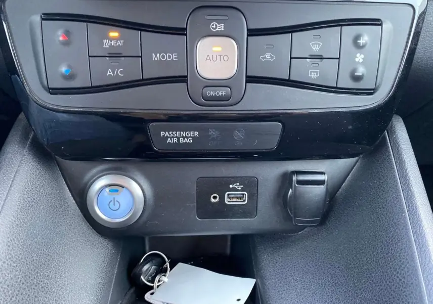 Détail de la console centrale du Nissan Leaf blanc 2020, montrant les commandes de climatisation et les ports USB et allume-cigare.