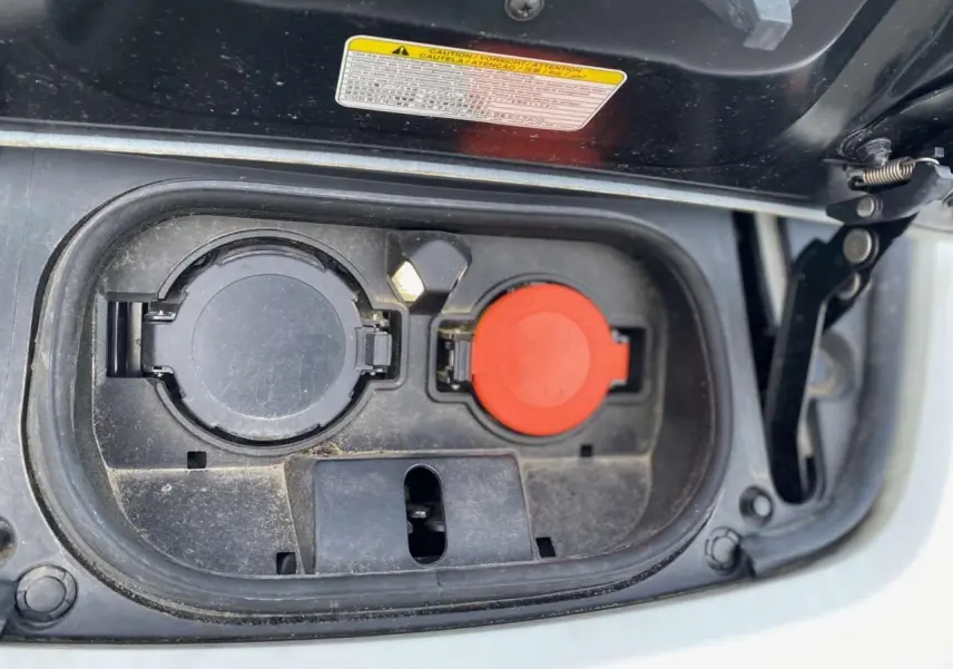 Prise de recharge électrique ouverte sur une Nissan Leaf blanche, vue rapprochée du compartiment de charge.