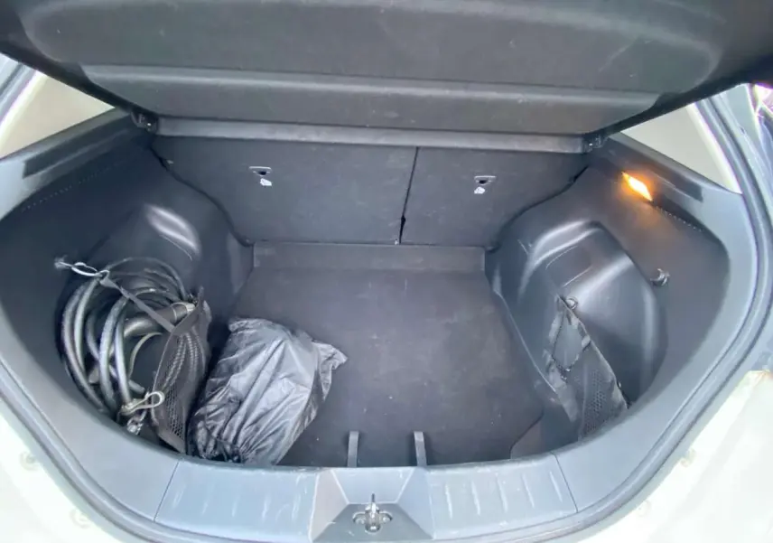 Coffre ouvert de Nissan Leaf blanche 2020, vue intérieure montrant un câble de recharge et un sac noir.
