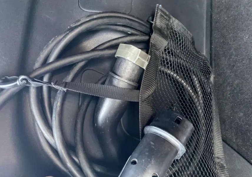 Gros plan sur le câble de recharge noir enroulé dans le coffre d'une Nissan Leaf blanche électrique.