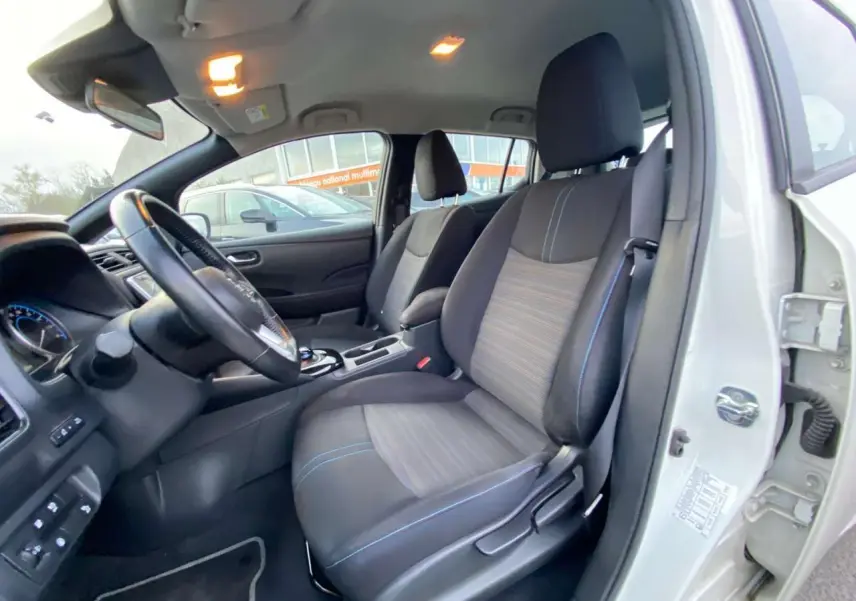 Vue intérieure côté conducteur du Nissan Leaf blanc 2020, sièges tissu noir avec surpiqûres bleues et tableau de bord visible.