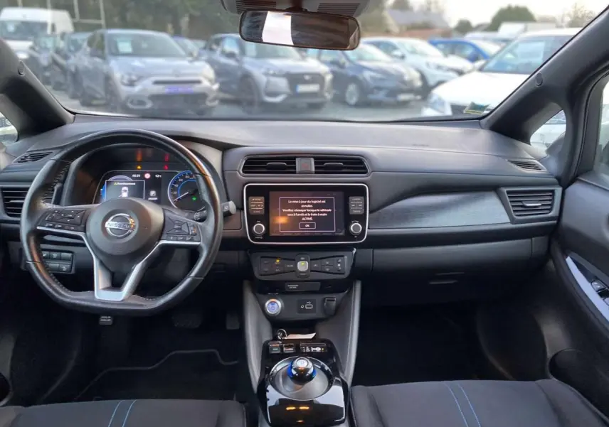 Vue intérieure avant du Nissan Leaf blanc 2020, tableau de bord avec écran tactile central et volant multifonction.