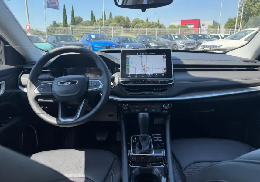 Vue intérieure avant du Jeep Compass 2025 avec tableau de bord noir et écran tactile central affichant une carte.