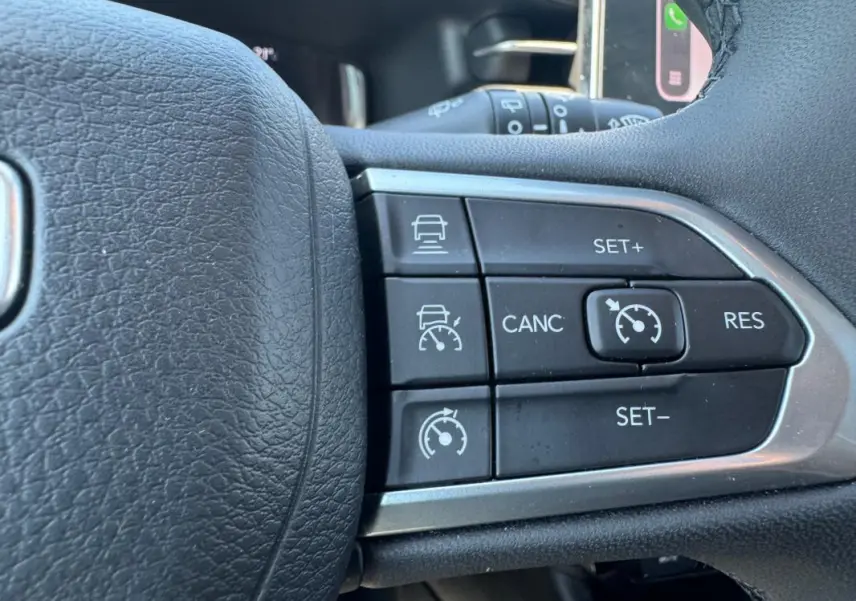 Gros plan sur les commandes du régulateur de vitesse au volant noir du Jeep Compass blanc 2025.