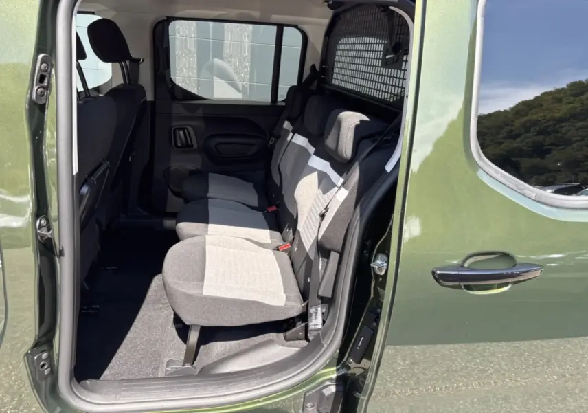 Vue latérale droite sur l'intérieur arrière du Citroën Berlingo Sirkka green, montrant les trois sièges indépendants et la grille de séparation.