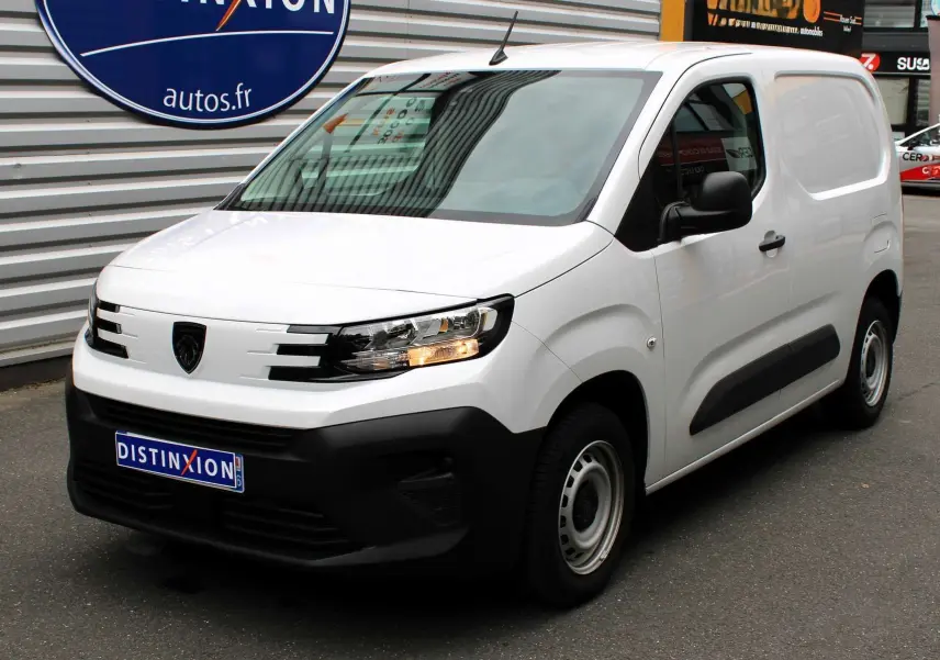 Peugeot Partner Fourgon blanc vue 3/4 avant droit avec calandre noire et feux allumés sur parking.
