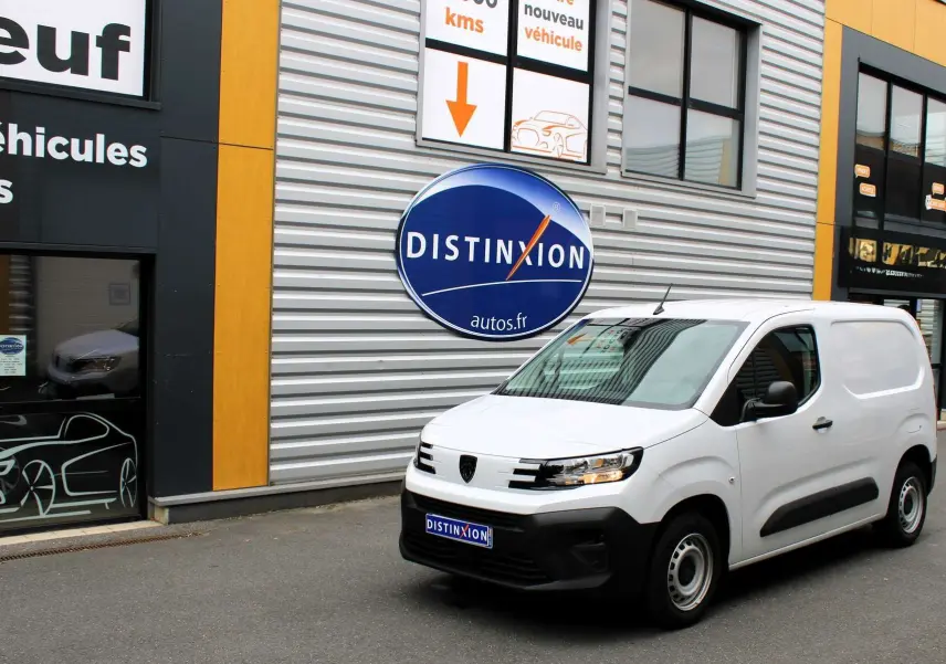 Peugeot Partner Fourgon blanc vu en 3/4 avant droit devant un bâtiment avec logo Distinxion.