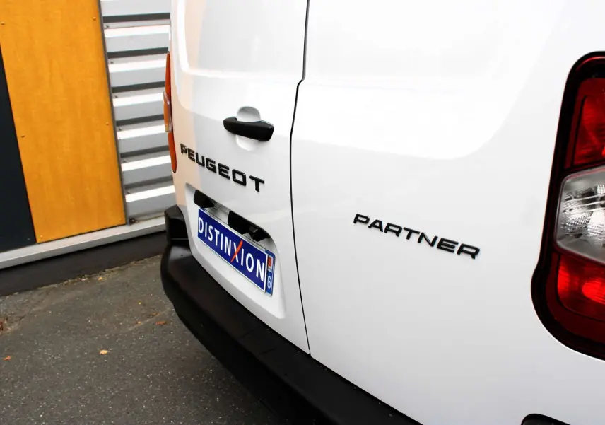 Vue arrière droite du fourgon blanc Peugeot Partner avec plaques d'immatriculation et feux arrière visibles.
